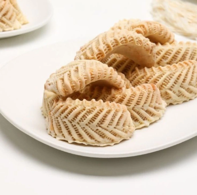 “A beautifully styled serving scene of Moroccan Gazelle Horns on an ornate Moroccan plate, sprinkled lightly with powdered sugar and topped with a few slivered almonds. Next to the plate, a traditional Moroccan teapot and mint tea glasses on a wooden or brass tray. Background hints of Moroccan patterns (tiles or textiles), warm golden tones, suitable as a final hero shot for a recipe blog.”